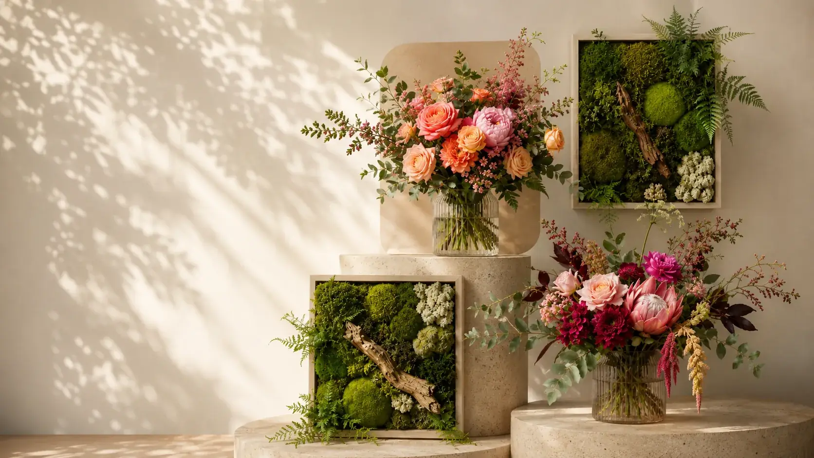Zwei gerahmte Moosbilder mit Farn und Treibholz, daneben zwei Sträuße mit Rosen, Dahlien und Protea in Glasvasen