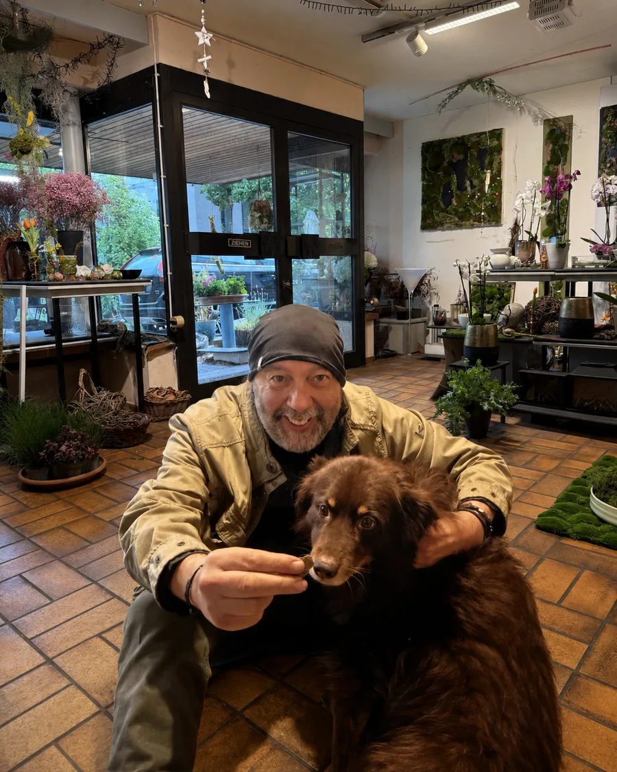 Jürgen Baumbach im Ladengeschäft, neben ihm sein Hund, im Hintergrund Moosbilder und Orchideen