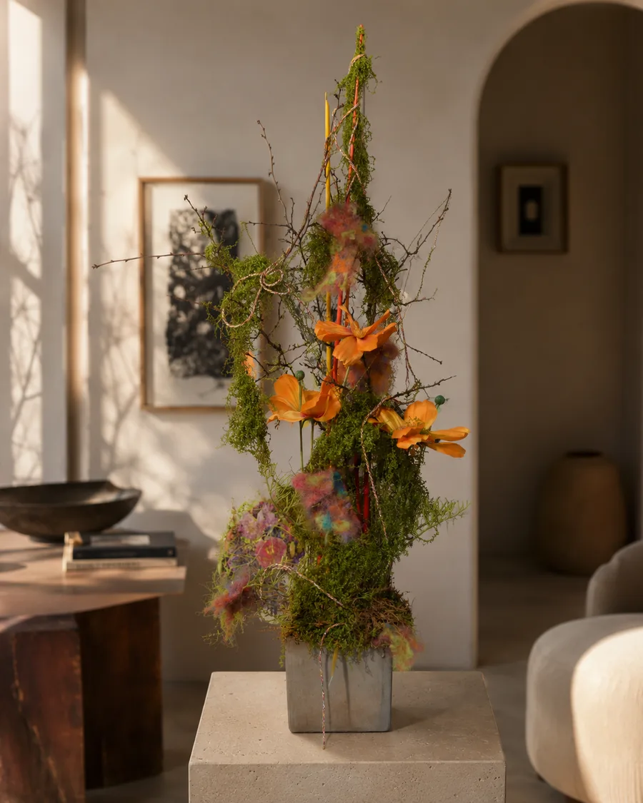 Hohe florale Säule aus Moos, Zweigen und orangen Blüten auf einem Sockel