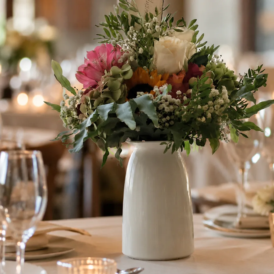 Tischgesteck in weißer Keramikvase auf gedecktem Tisch mit Kerzen und Weingläsern